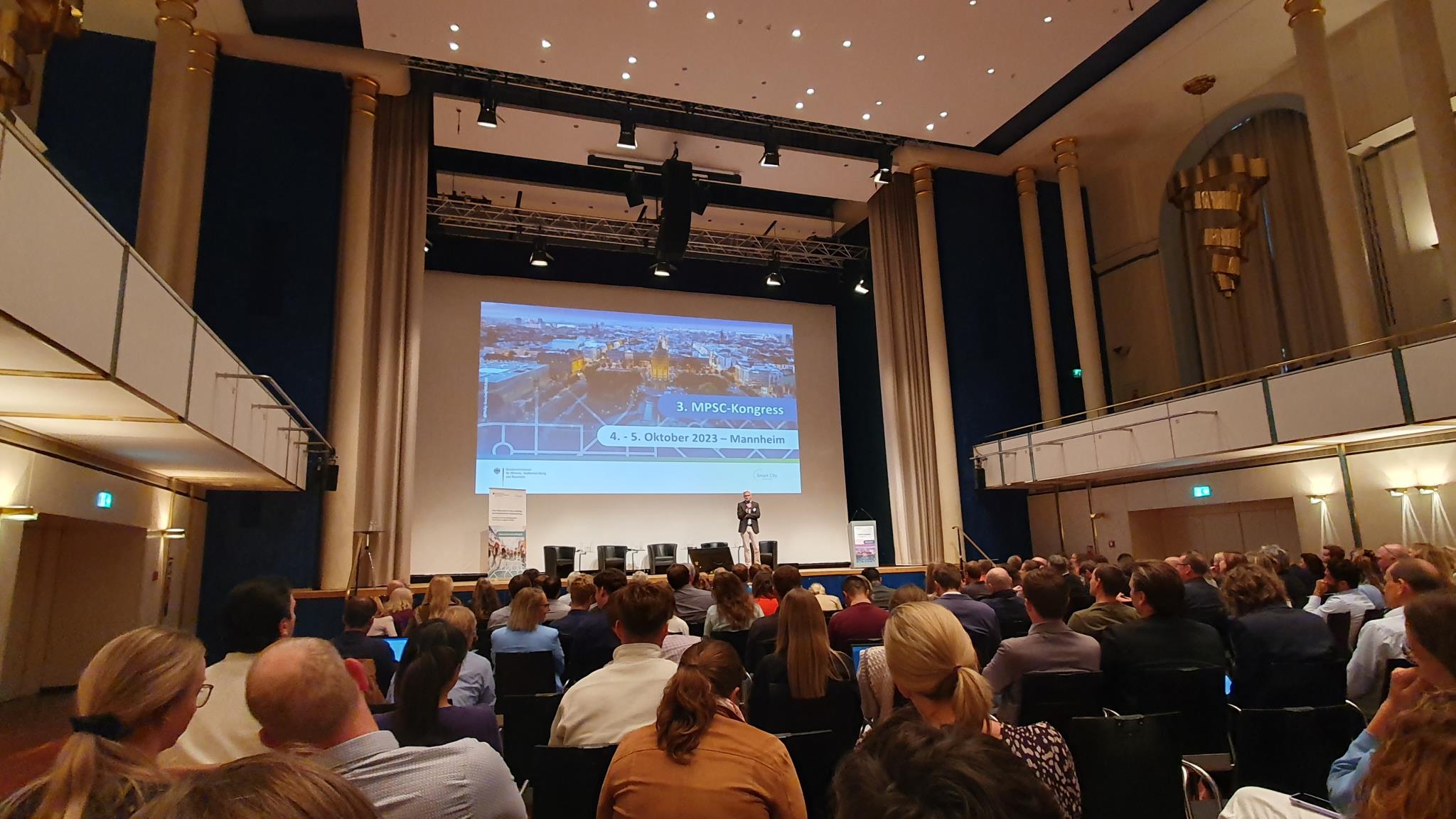 Foto: Veranstaltungssaal mit Blick auf Bühne und Hinterköpfe des Publikums