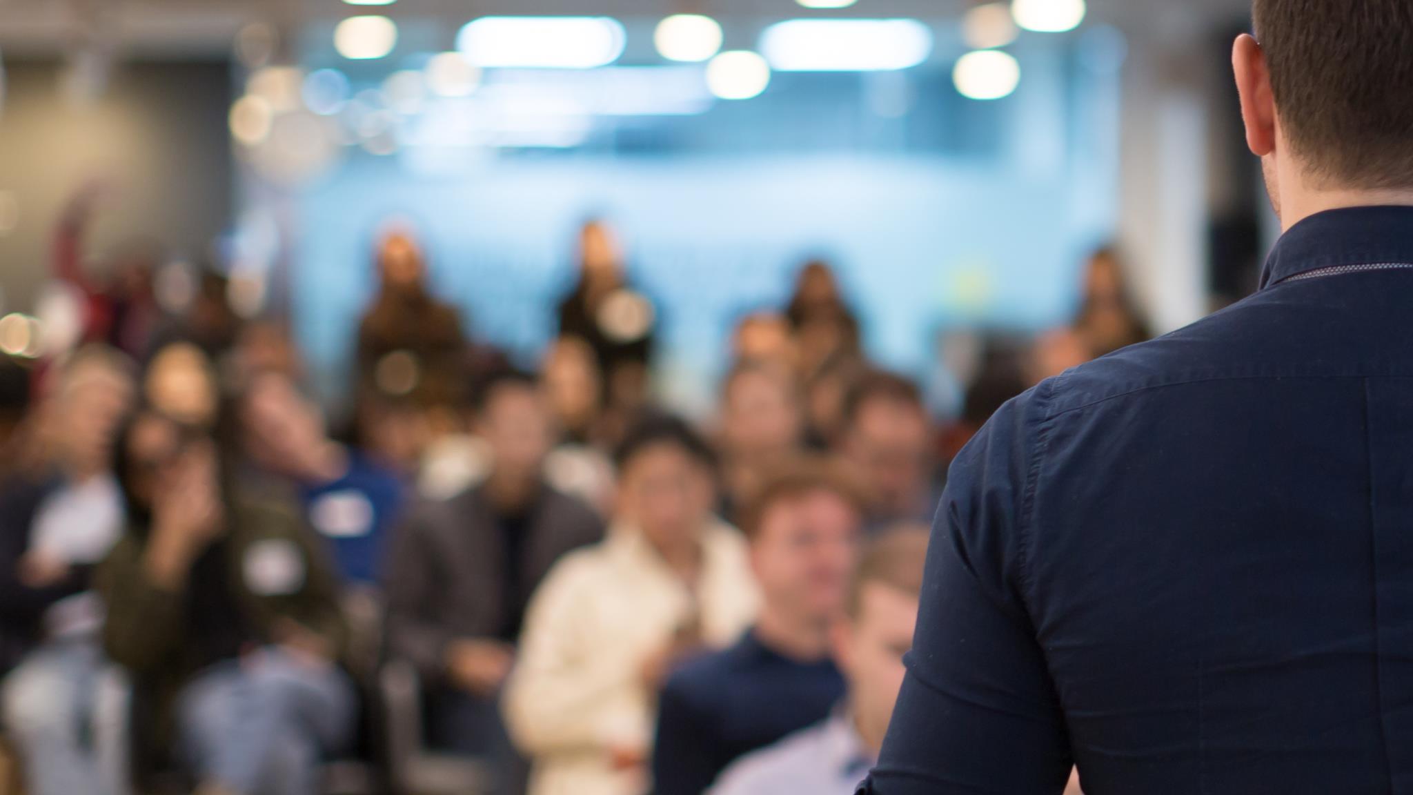 Foto: Mann steht vor Publikum auf Veranstaltung, Blick über Schulter