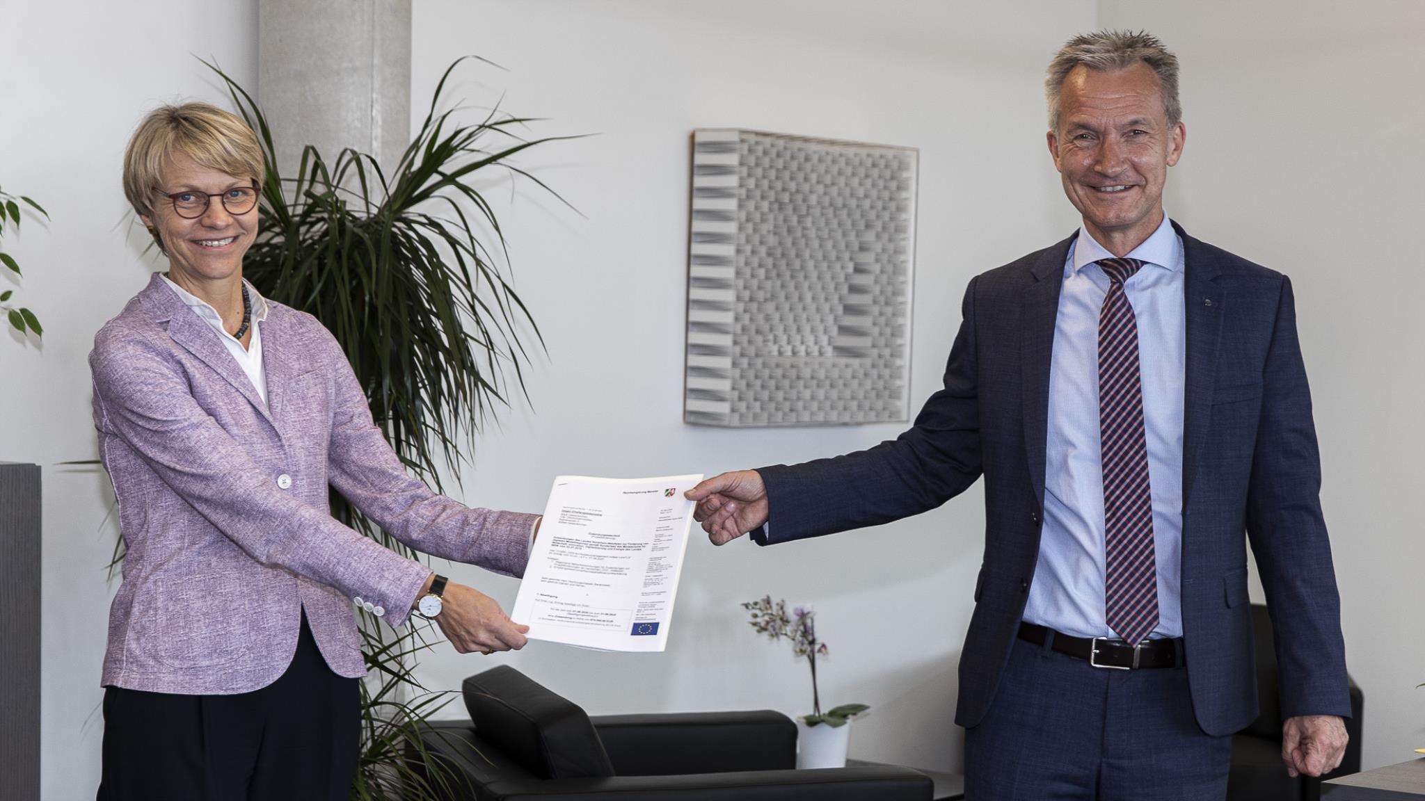 Das Bild zeigt Regierungspräsidentin Dorothee Feller, die ein Dokument an Oberbürgermeister Frank Baranowski übergibt.