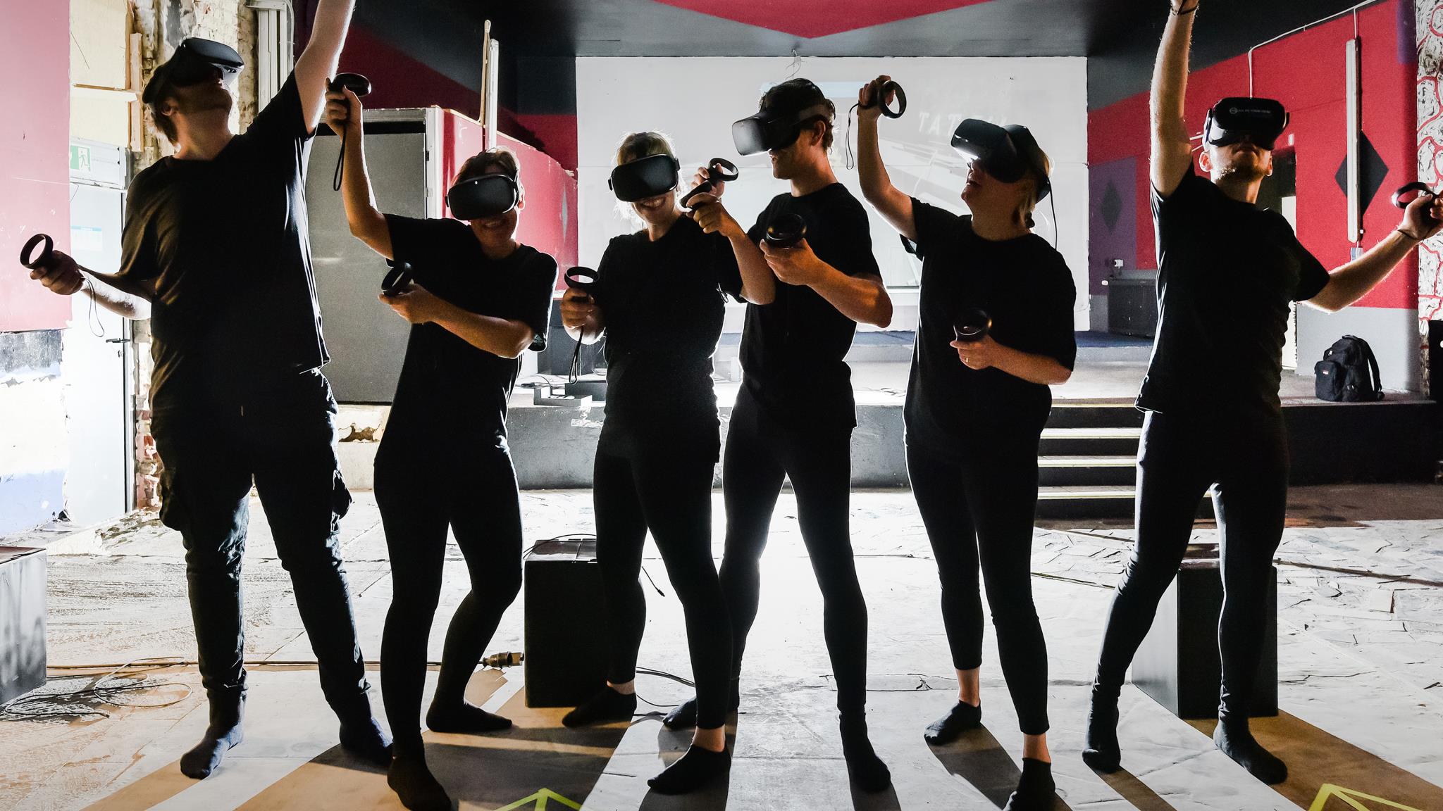 Foto: Mehrere schwarzgekleidete Personen mit VR-Brillen stehen in einer Reihe machen verschiedene Bewegungen.