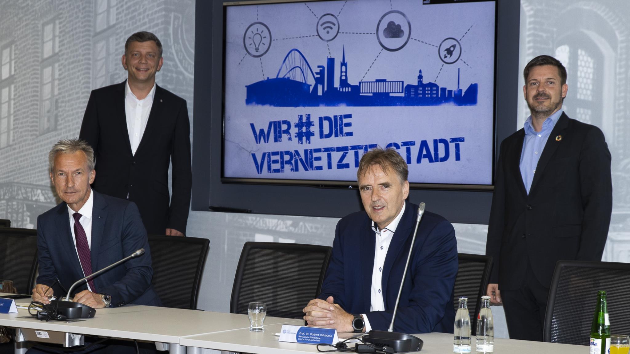 Vier Personen stehen und sitzen vor einem Monitor