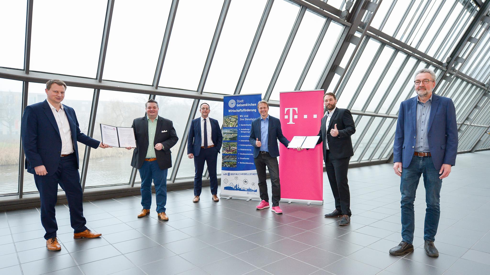 Sechs Männer stehen in einer Halle neben zwei Aufstellern zur Stadt und zur Telekom.